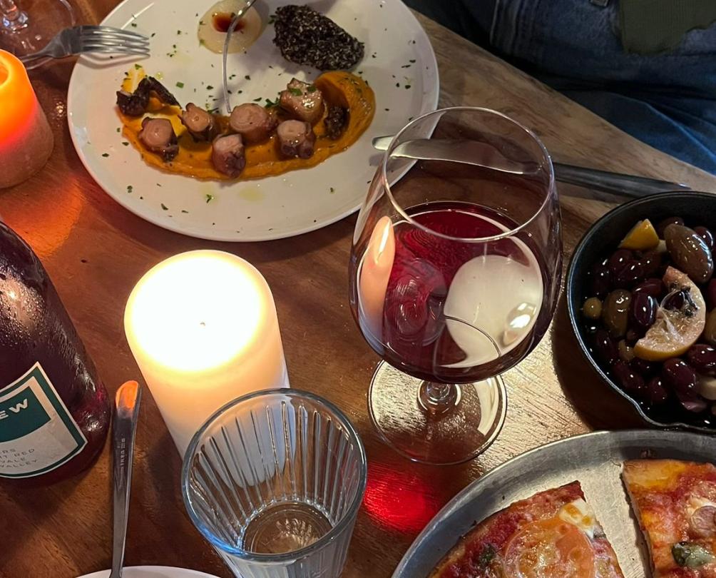 A candelit table in a restaurant filled with wine, pizza, and pasta.