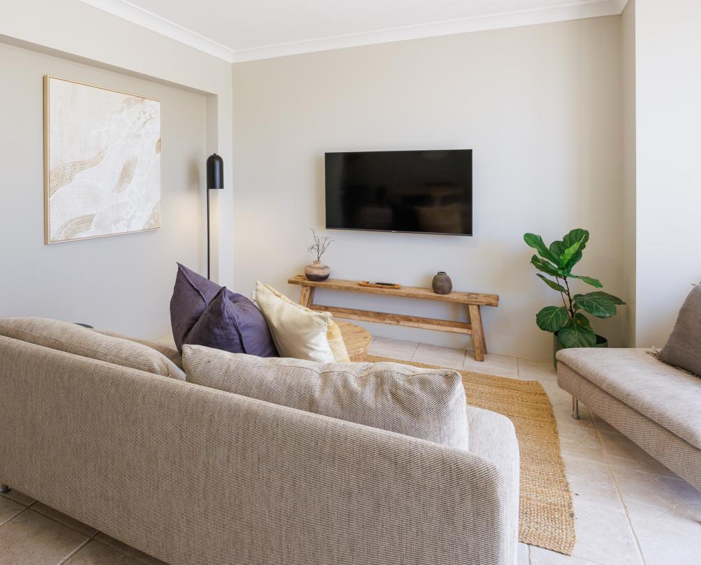 A living room with comfortable grey lounge and a TV on the wall.
