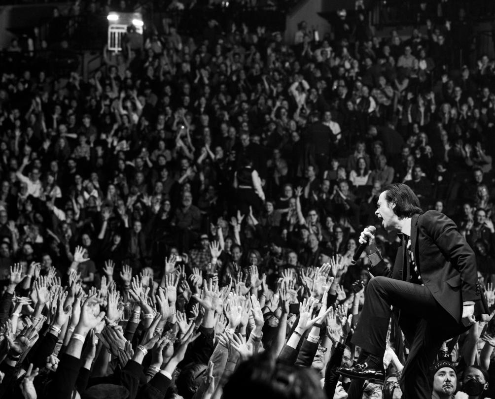 A black and white photo of a man in a black suit performing in front of a huge crowd.