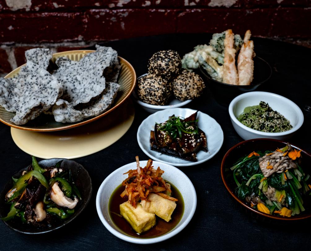 A dark table in front of a dark brick wall filled with various Asian dishes.
