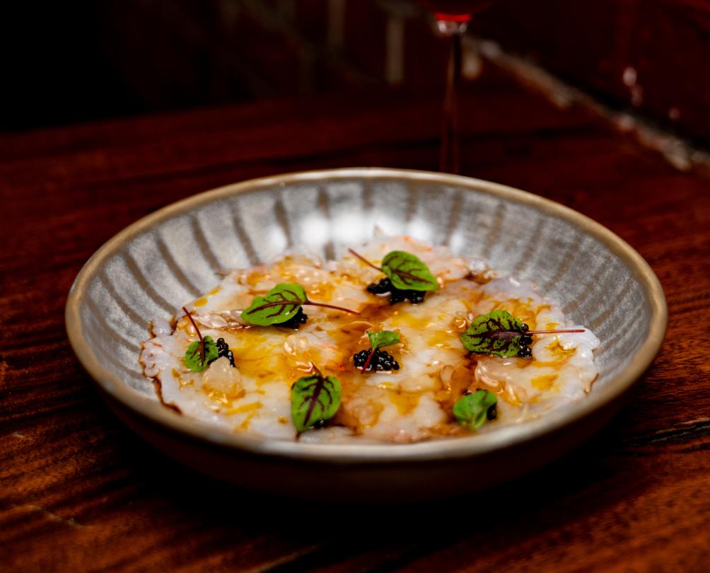 A grey plate filled with golden sashimi and microherbs on a wooden table.