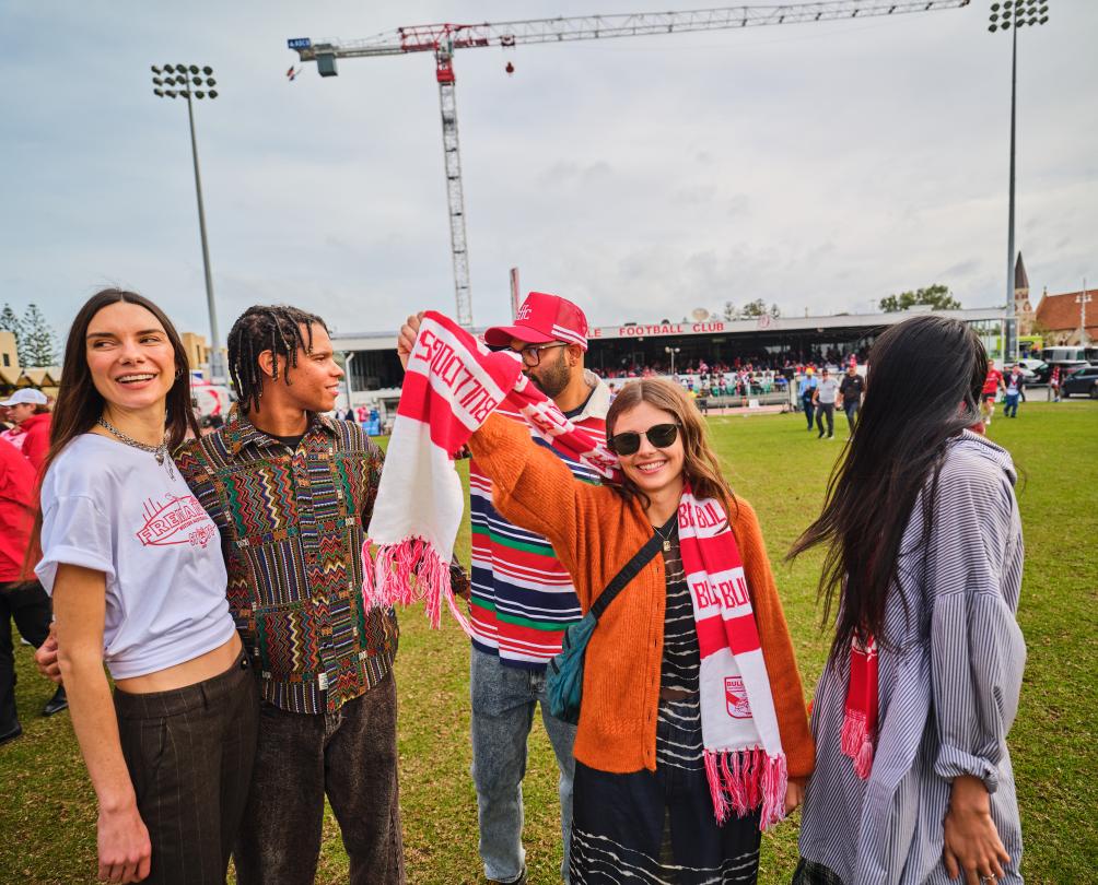 A group of friends on an oval celebrating after a football match.