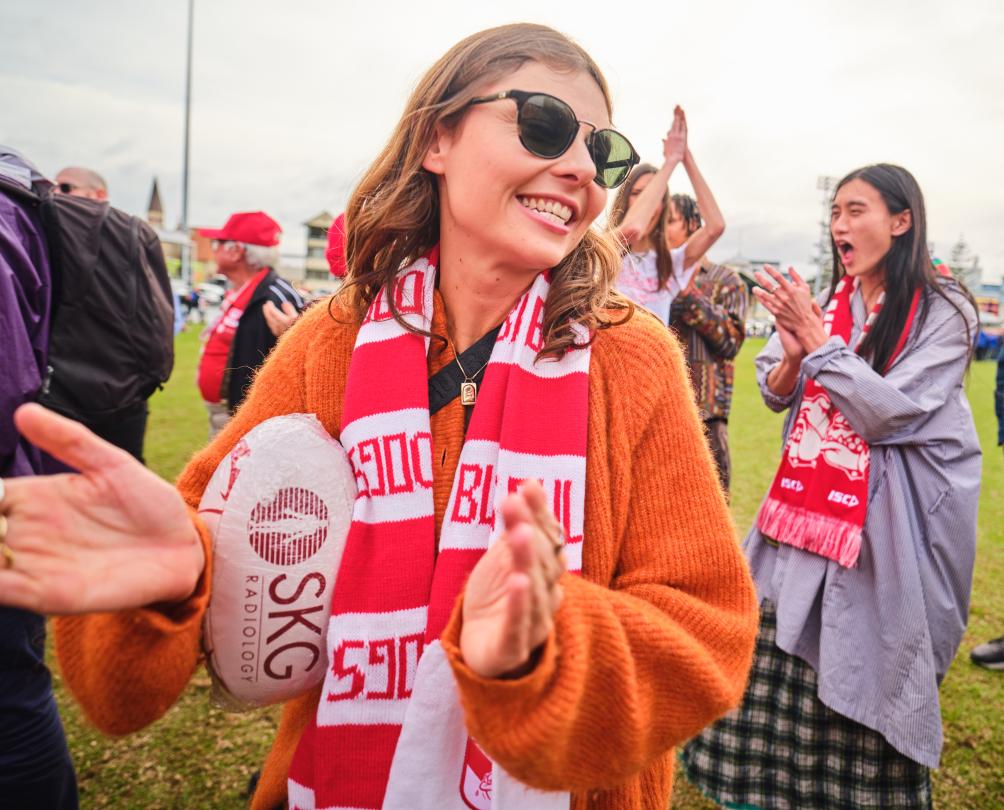 A woman in a red and white scarf claps her hands while holding a white football.