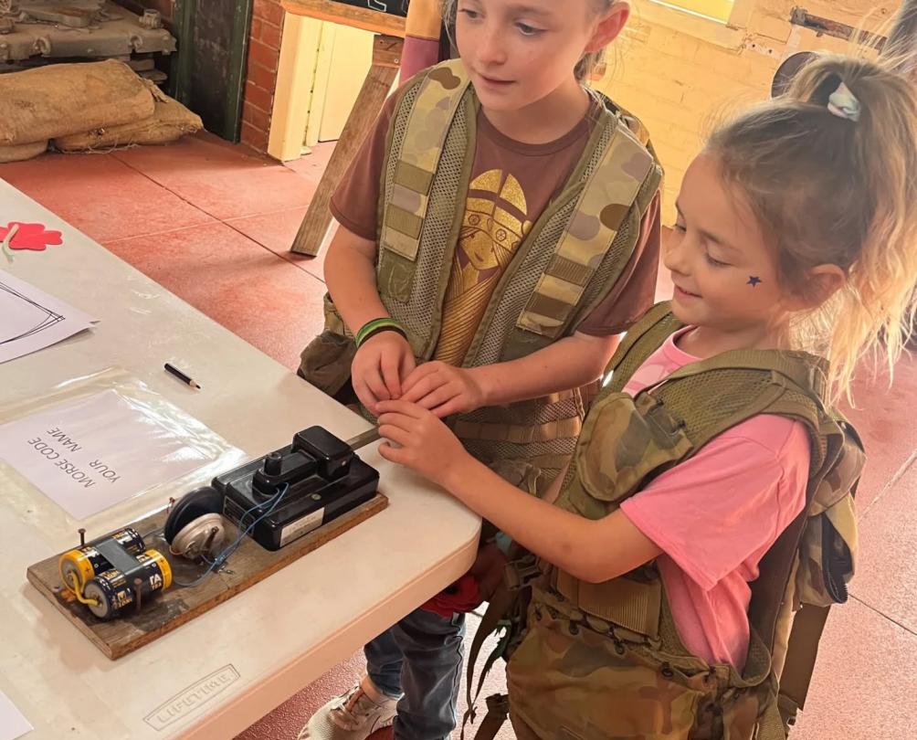Two girls dressed in army costumes practice using morse code.