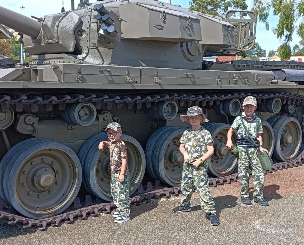 Three young children dressed in army costumes pose in front of an army truck.