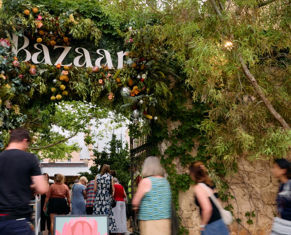 People walk beneath a big green archway with the words Bazaar above.