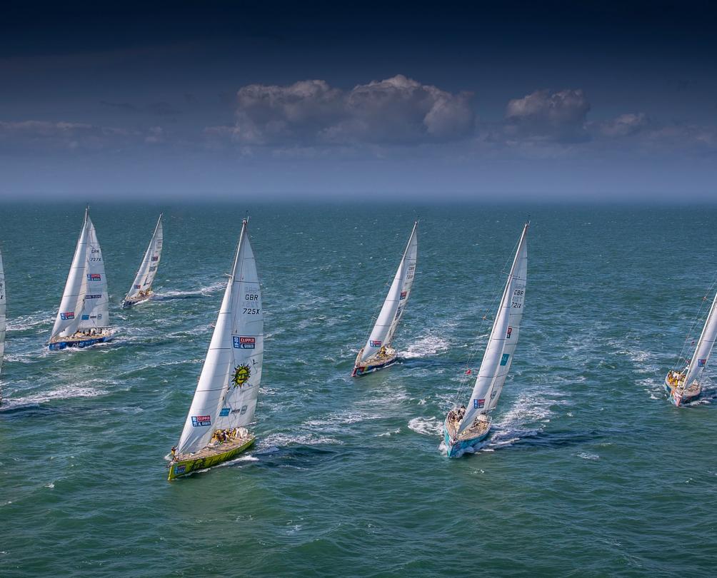 A fleet of yachts race across a bright blue ocean.