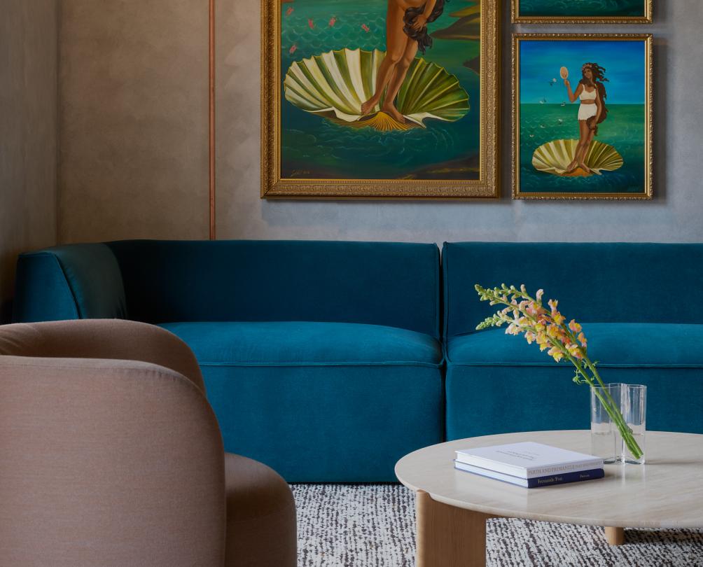 A hotel lobby with plush blue furniture and statement art on the wall depicting a woman in a clam shell.