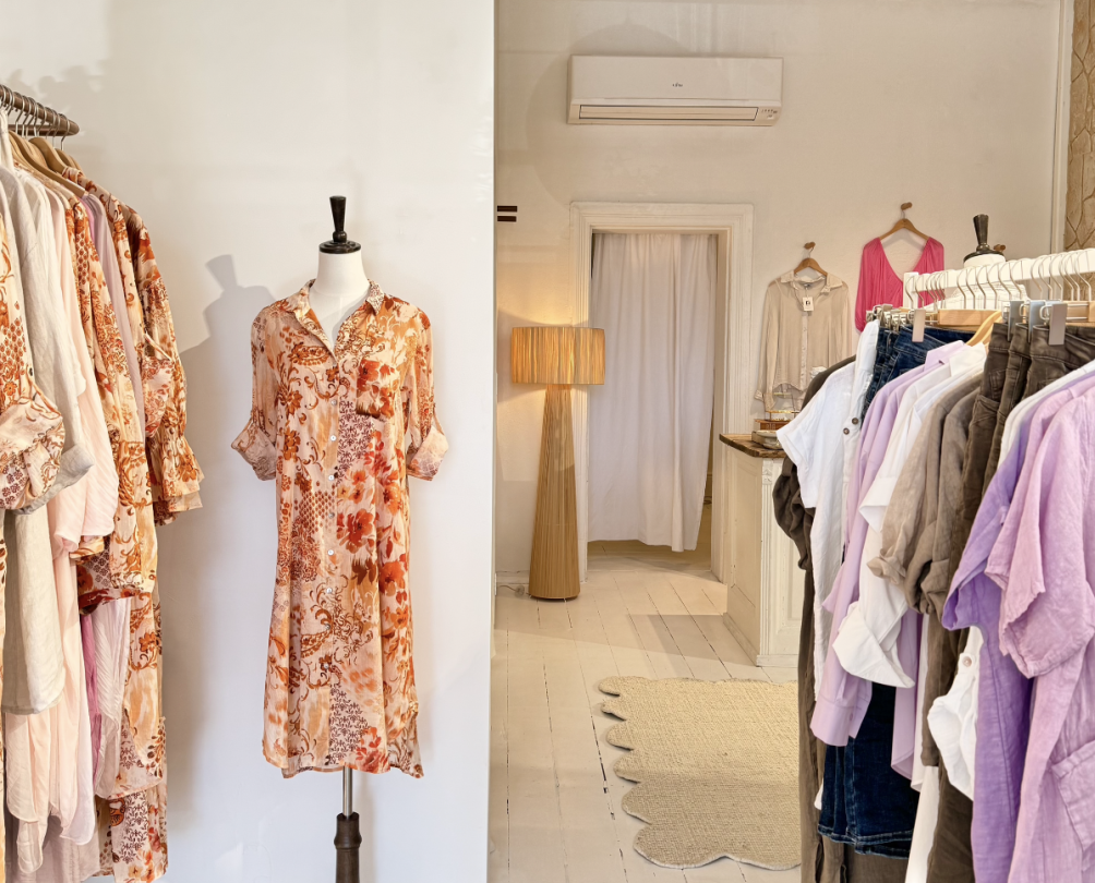The interior of a clothing store featuring dresses in lilac and orange.
