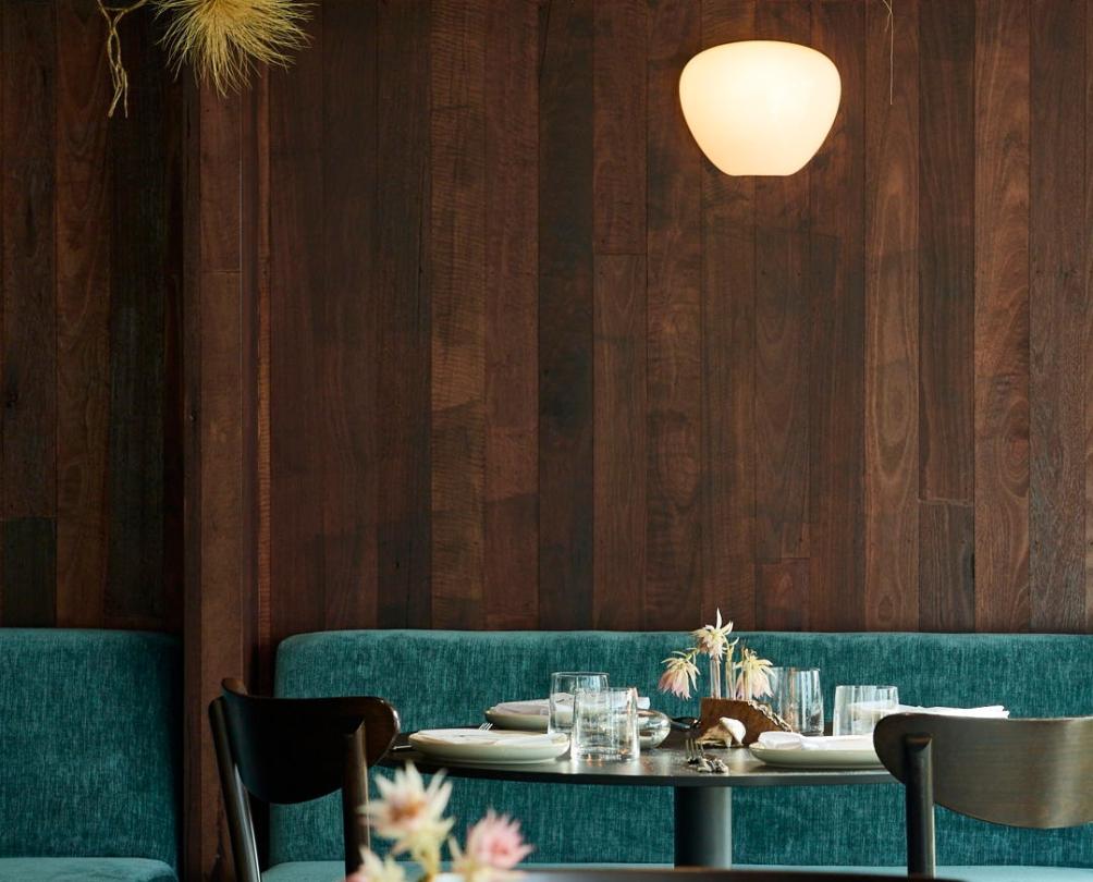 A dark wood panelled dining room with dark wooden tables and chairs and teal lounges.