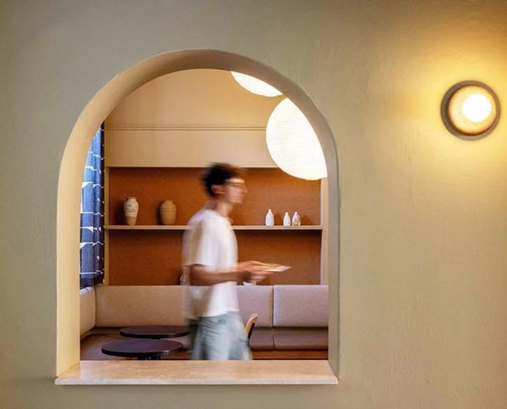 A young man carrying a plate is seen through an arch window.