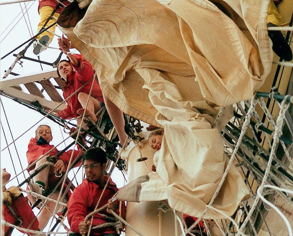 A crew putting up a sail on a tall ship.