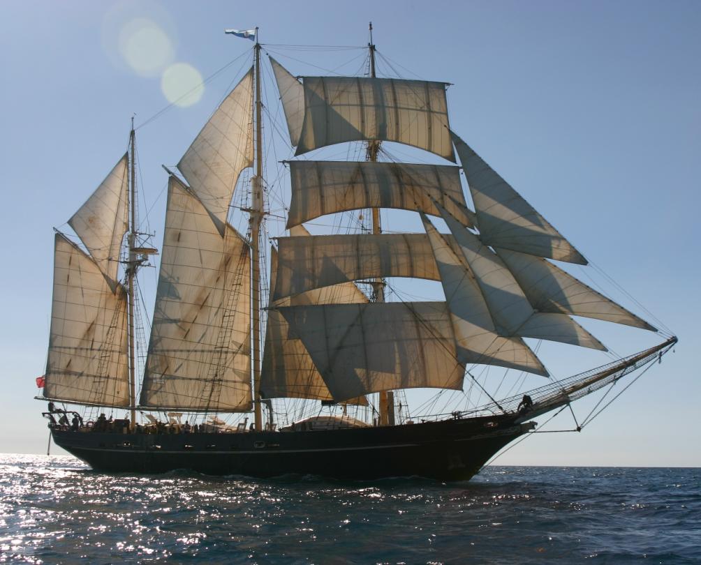 A tall ship with several masts sails on the ocean under a blue sky.
