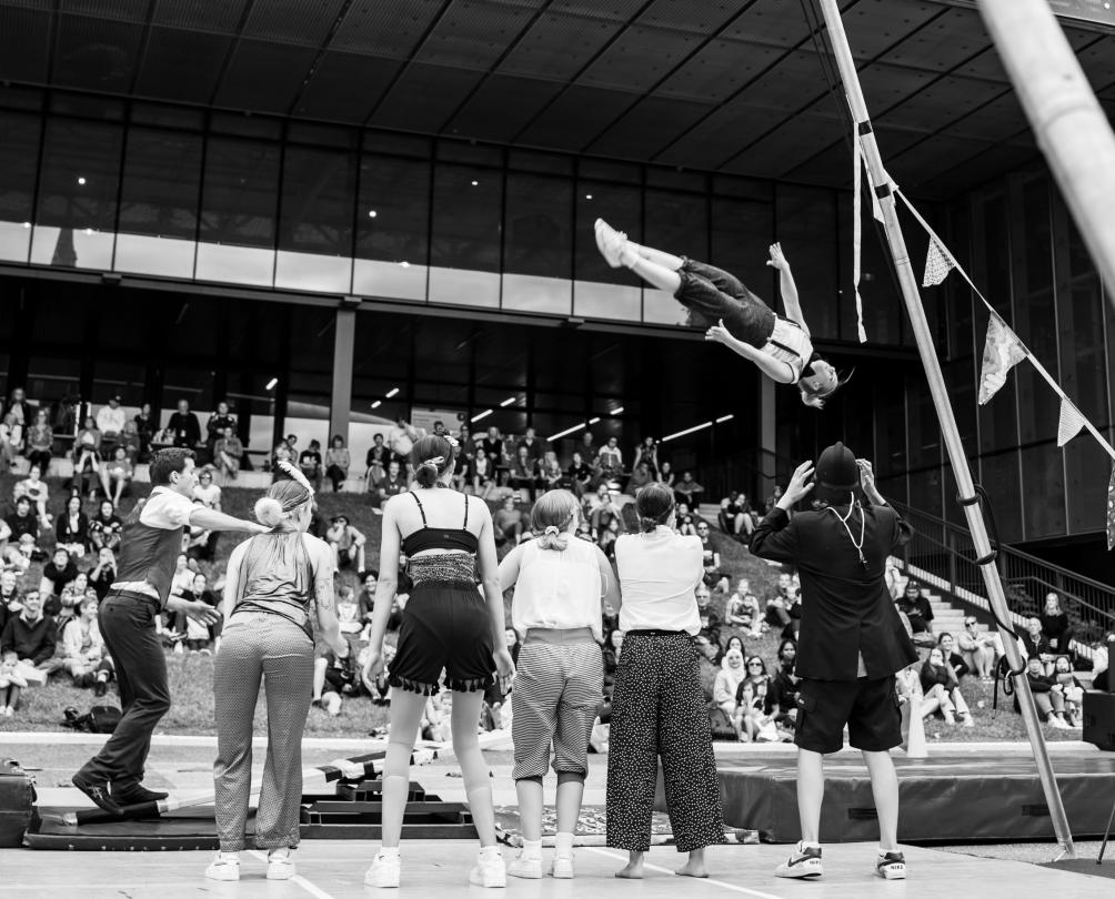 A group of circus performers perform outside a crowd on a hill.