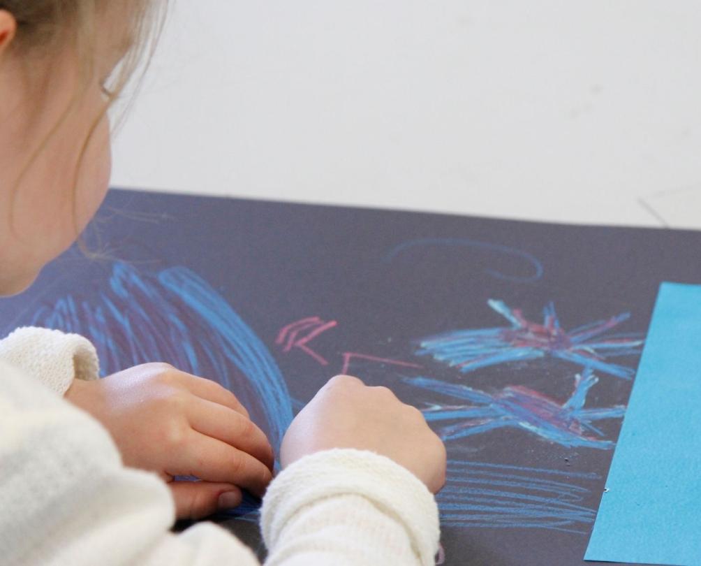 young child drawing on black paper 