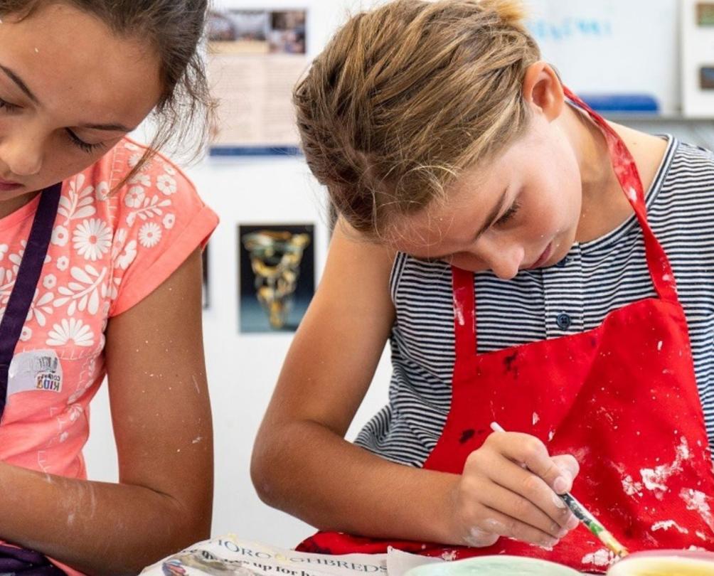 two girls doing art sitting together with aprons 