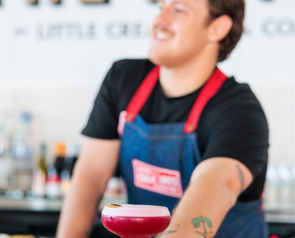 a server with a pink cocktail in a martini glass behind the bar 