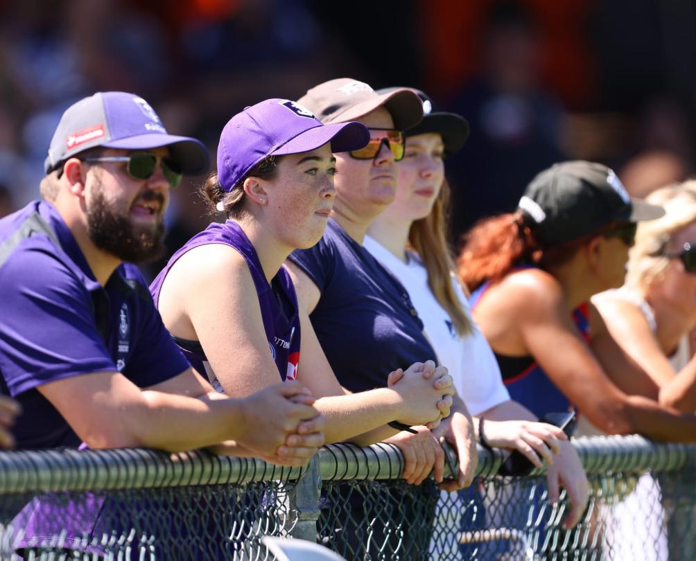 a group of fans in purple Dockers gear watching over a fence at the Fremantle Oval 