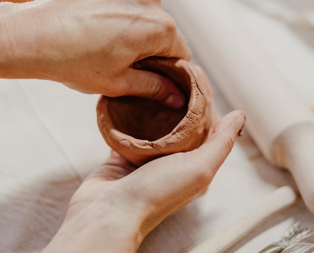 hands shaping a clay cup at a table