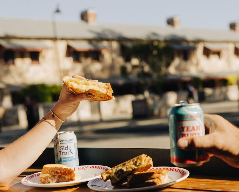 some toasties and two gage roads beer on a bench with the Warders hotel in the background
