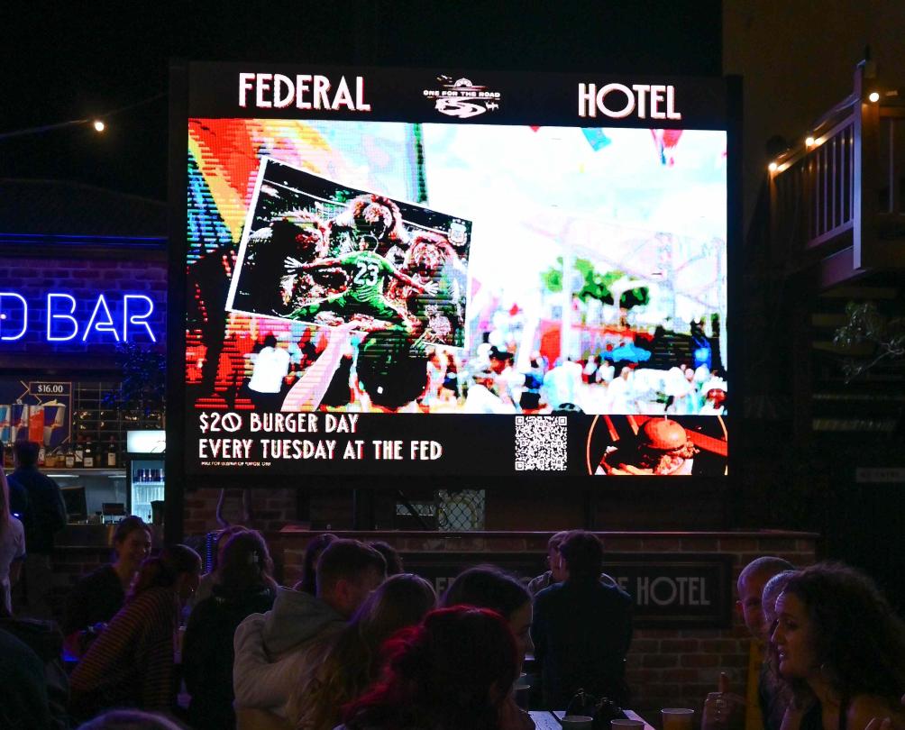 a TV screen at the Federal Hotel with fans watching 
