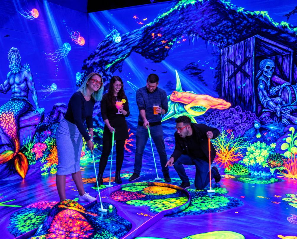 a group of mates doing mini golf in a glow in the dark mini golf course