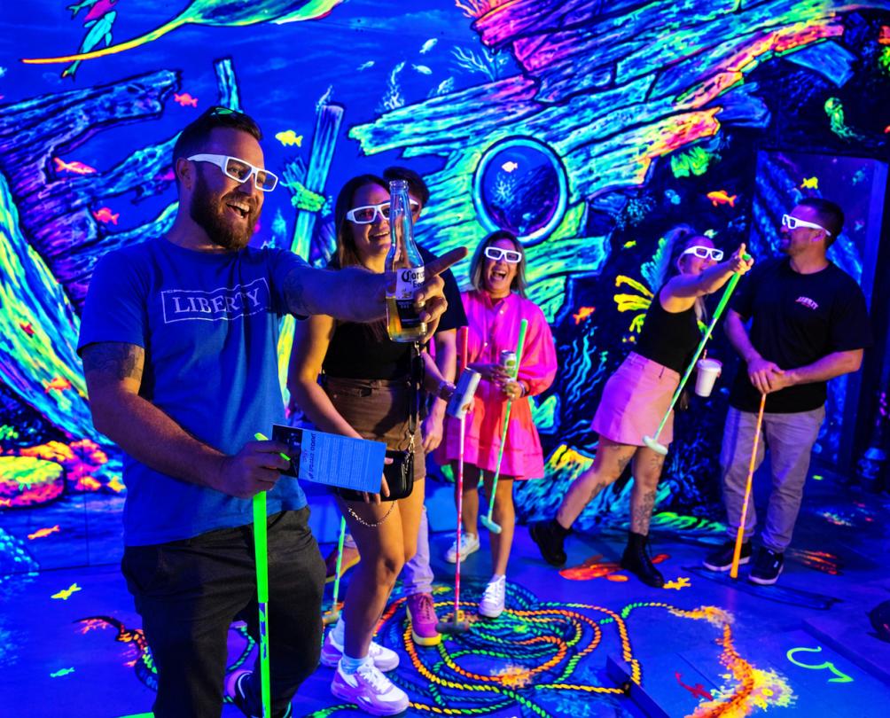 a group of people inside a glow in the dark Putt Putt at Glowing Rooms mini golf 