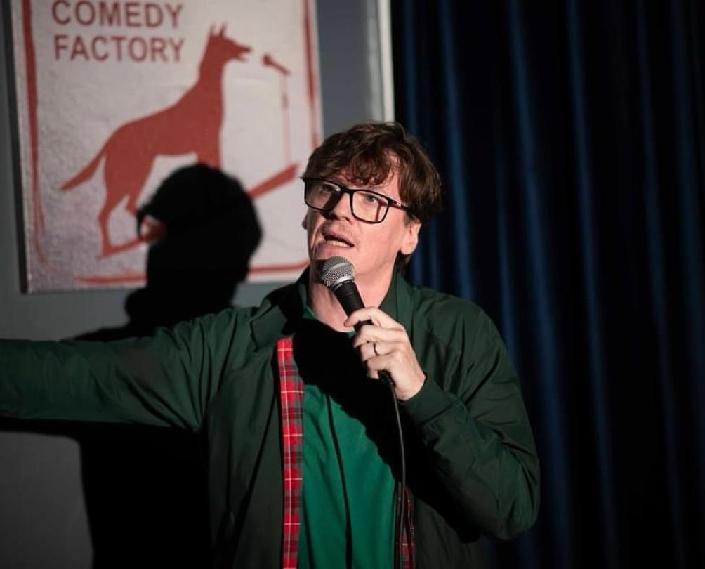 a man with glasses on a stage with a mic