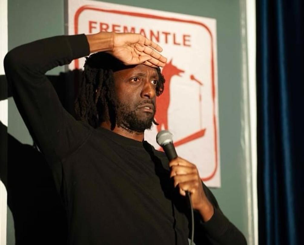 a man on a stage with a microphone shielding his eyes