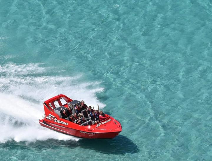 red jet boat glides through clear turquoise water leaving white wake