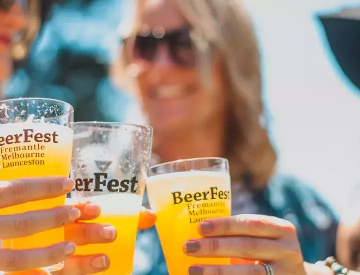 three people smiling outdoors in the sunshine holding cold beers