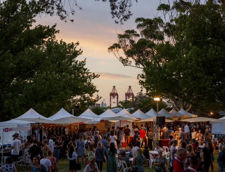 crowd of people shopping pop up tent stores at Bazaar at Fremantle Arts Centre with the port's cranes in the background
