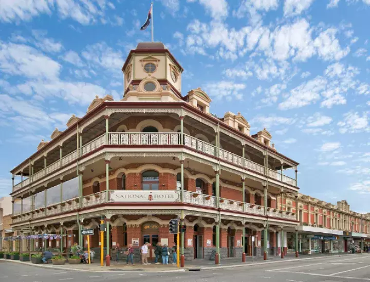 The National Hotel in Fremantle against a blue sky dotted with white clouds. Visitors standing at the front doors. 