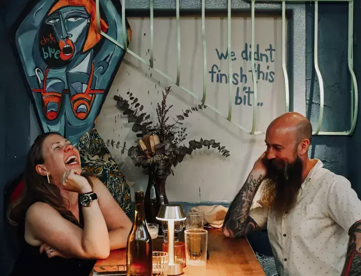 A couple laughing over dinner inside a restaurant.