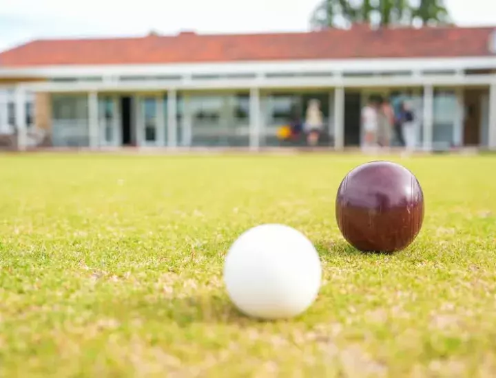 A lawn bowls ball and puck on a green lawn with a clubhouse in the background.