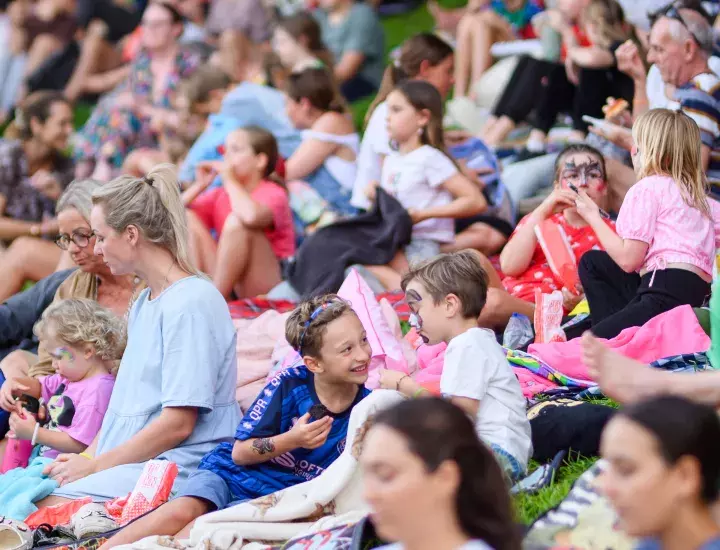 A large group of families sitting on picnic blankets on a sloped lawn.