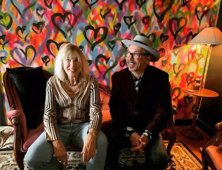 A man and woman sit in front of a brightly coloured wall in a cosy room.