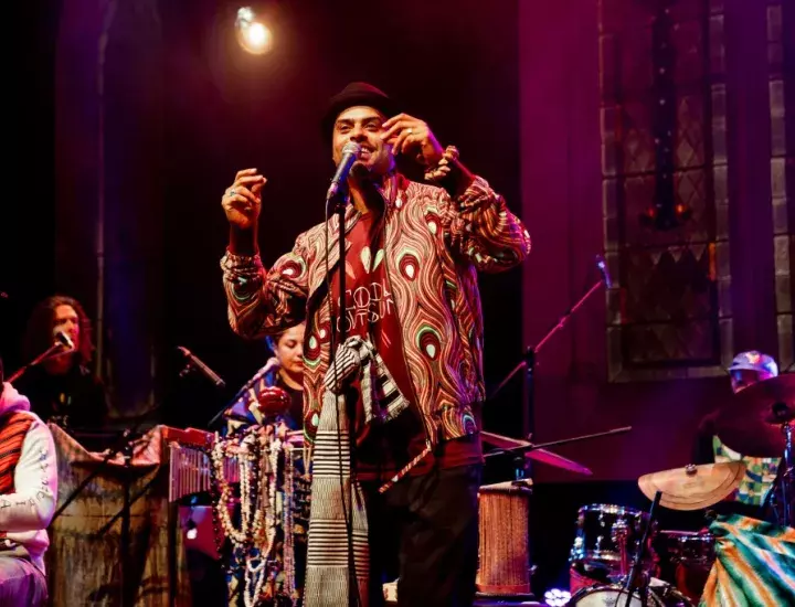 A man in colourful dress singing behind a microphone on a purple stage.