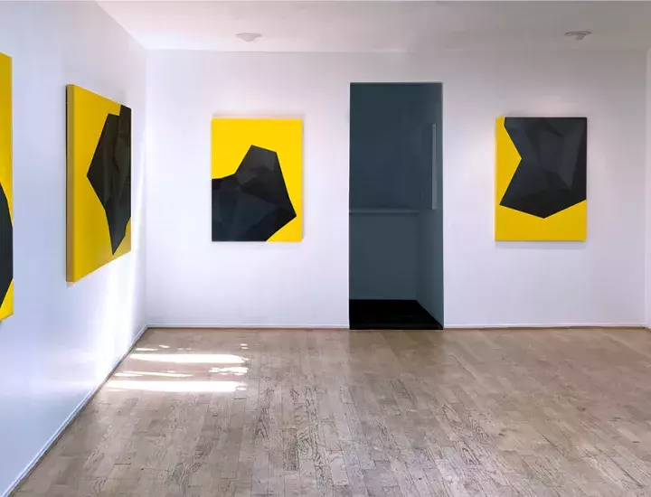 A small gallery room with bold geometric yellow and black artworks along the walls.
