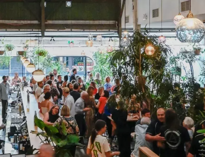 A large bar and dining room with lots of greenery and colourful lights hanging from the ceiling, with lots of people socialising below.