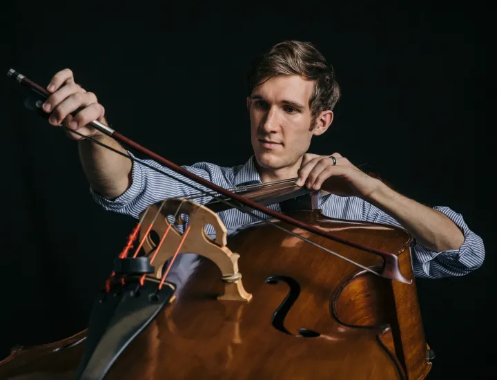 a man playing a cello in a blue shirt with a black backgroun