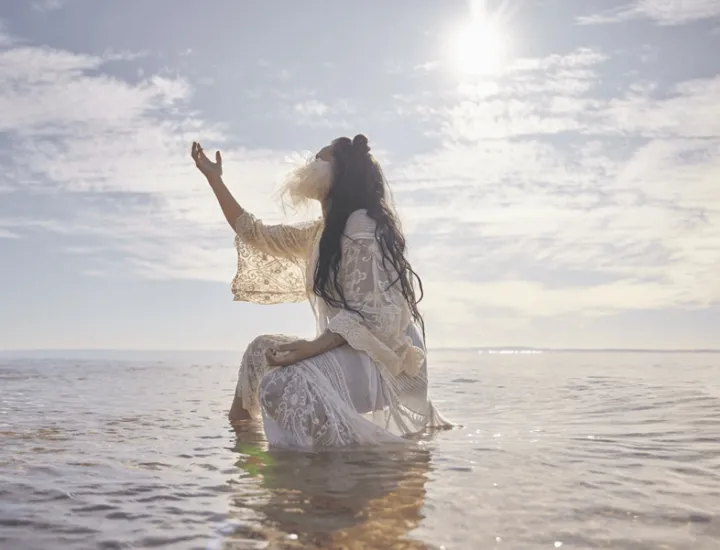 a woman in the water reaching up to the sun 