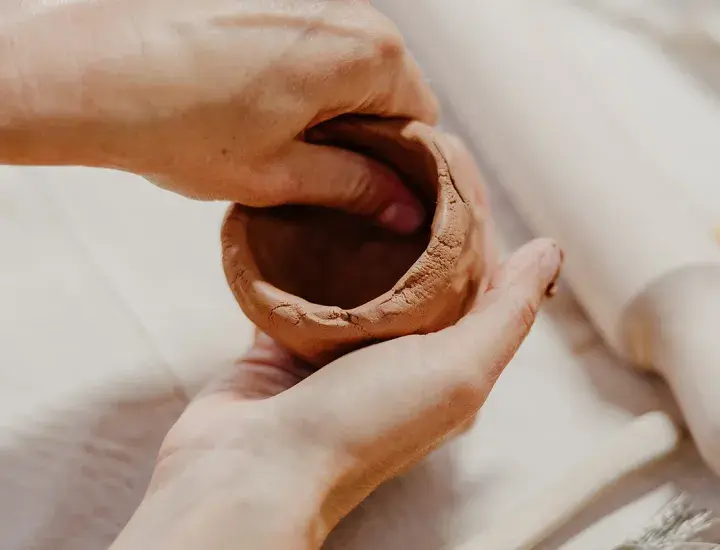 hands shaping a clay cup at a table