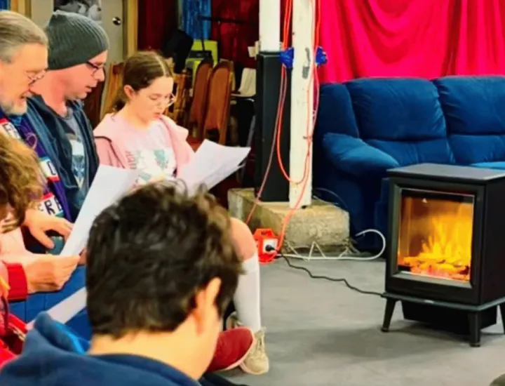 a choir in a comfy living room with a fire singing 